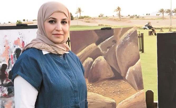 د. منى عبدالباري أمام لوحتها للصخور حكاية في الملتقى﻿