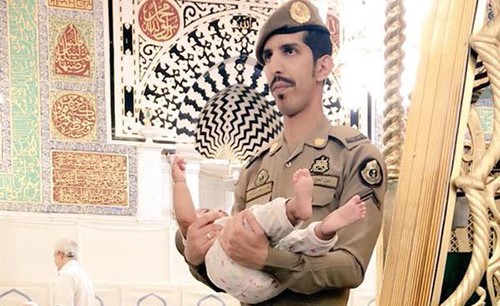 شاهد.. صورة لعسكري سعودي يحمل طفلا  بالمسجد النبوي كي يتمكن والده من الصلاة