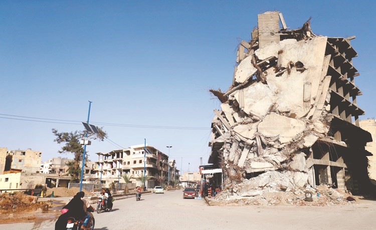 سوريون يمرون بدراجاتهم البخارية أمام مبنى مدمر في الرقة امس الاول	(أ ف پ)﻿