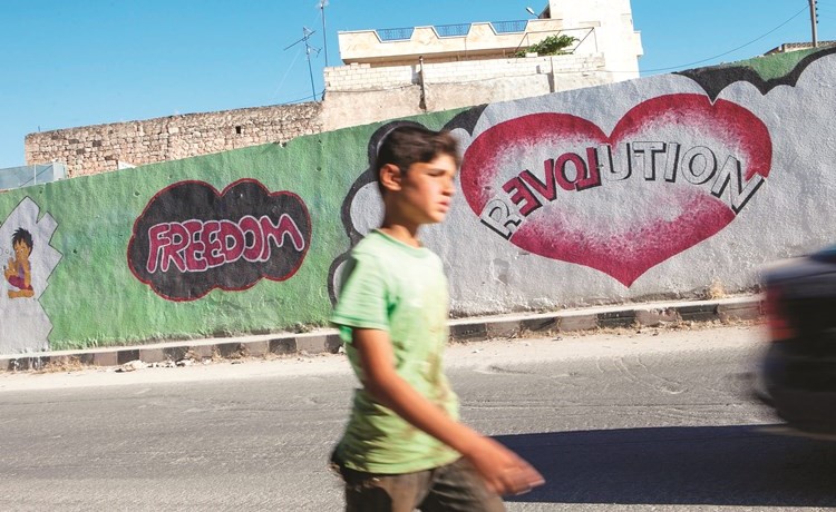 طفل سورية يمر امام جدارية في كفرنبل	(أ.ف.ب.)﻿
