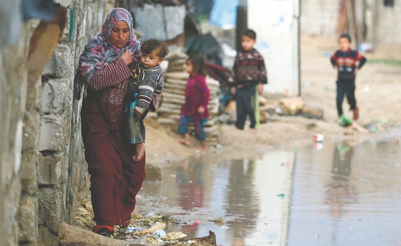 سيدة فلسطينية تعبر بأبنائها تحت المطر في مخيم خان يونس بغزة امس الاول	(رويترز) ﻿