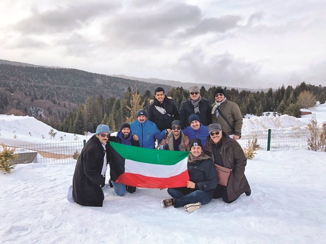 عدد من المشاركين في الرحلة يرفعون علم الكويت على أحد الجبال﻿