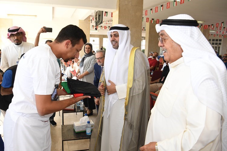 أحد الشباب يتسلم علم الكويت من الوزير محمد الجبري بحضور اللواء فهد الفهد﻿