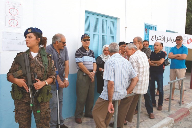 تونسيون ينتظرون دورهم بحراسة الجيش أمام احد مراكز الاقتراع في سوسة	(رويترز)﻿