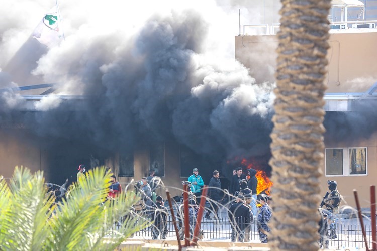محتجون عراقيون يضرمون النار في إحدى بوابات السفارة الاميركية ببغداد قبل انسحابهم من محيطها امس(رويترز) ﻿