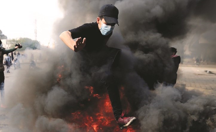 محتج عراقي يقفز لتجاوز النيران المشتعلة نتيجة حرق المتظاهرين اطارات السيارات لقطع طريق ببغداد أمس 	 (رويترز)