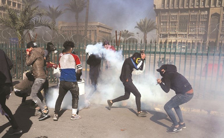 متظاهرون يحتمون من قنابل الغاز المسيلة للدموع خلال مواجهات مع الأمن ببغداد (رويترز)