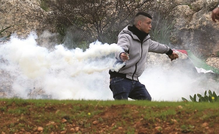 فتى فلسطيني يرمي قنبلة غاز مسيلة للدموع خلال مواجهات مع حرس الحدود الاسرائيلي في الضفة (أ.ف.پ)