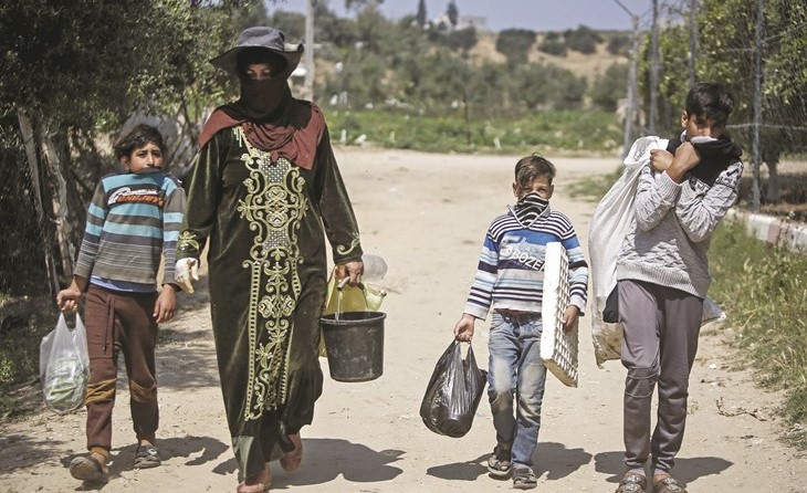 أفراد عائلة فلسطينية ترتدي أقنعة واقية ضد كورونا في طريقهم للمنزل بعد يوم عمل شمالي غزة أمس	(ا.ف.پ)