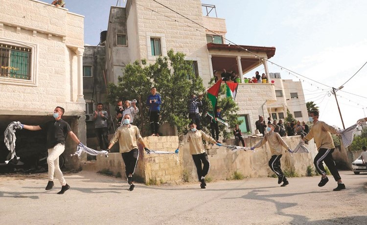 شباب فلسطينيون يؤدون الدبكة بالقفازات والكمامات محافظين على التباعد الاجتماعي لتسلية المحجورين في قرية الترقومية بالخليل في الضفة الغربية (أ.ف.پ)