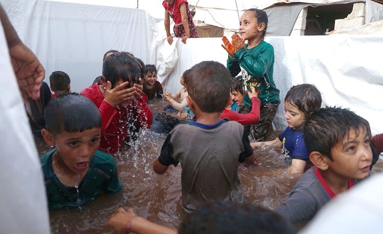 اطفال يلعبون بالماء في حوض بدائي على ظهر شاحنة لتخفيف الحر في مخيم كللي بادلب	(أ.ف.پ)