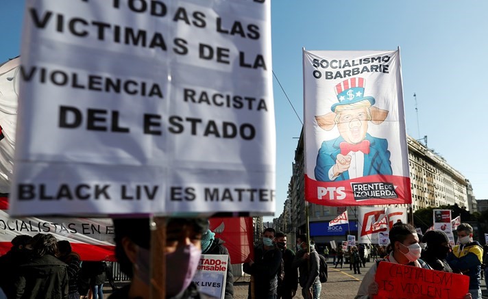محتجون يحملون صورة ساخرة للرئيس دونالد ترامب ولافتة تندد بعنف الشرطة وعنصريتها في بوينس ايرس بالارجنتين	(رويترز)