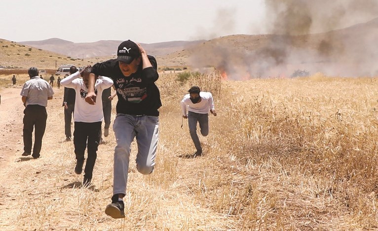 فلسطينيون يحتمون من قنابل الغاز التي يطلقها الاحتلال تجاههم خلال احتجاجات على ضم الضفة في بلدة العطوف في غور الاردن	(ا.ف.پ)