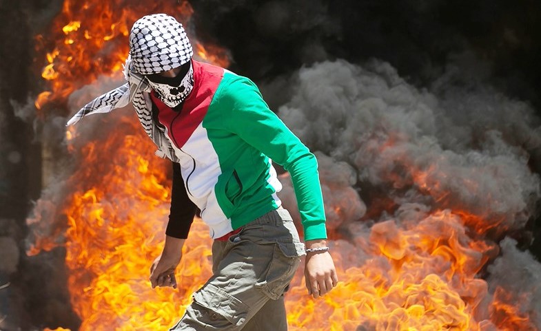 فلسطيني يسير بجانب إطارات مشتعلة بمظاهرة في الضفة ضد خطط الاحتلال لضمها	(أ.ف.پ)