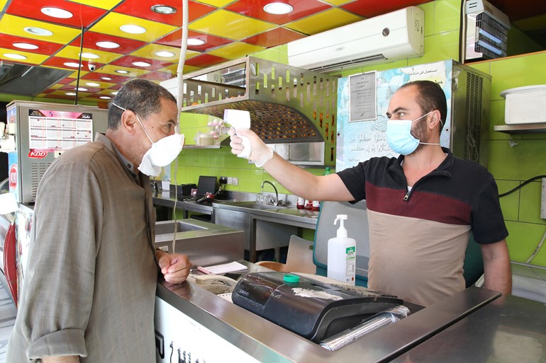 مثنى الحلقي يقيس درجة حرارة أحد الزبائن