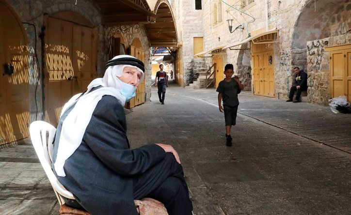 فلسطيني مسن يمر بجواره أطفال بأحد شوارع مدينة الخليل في الضفةامس حيت تعتزم اسرائبل ضم مزيد من الأراضي مطلع يوليو المقبل(أ.ف.پ)
