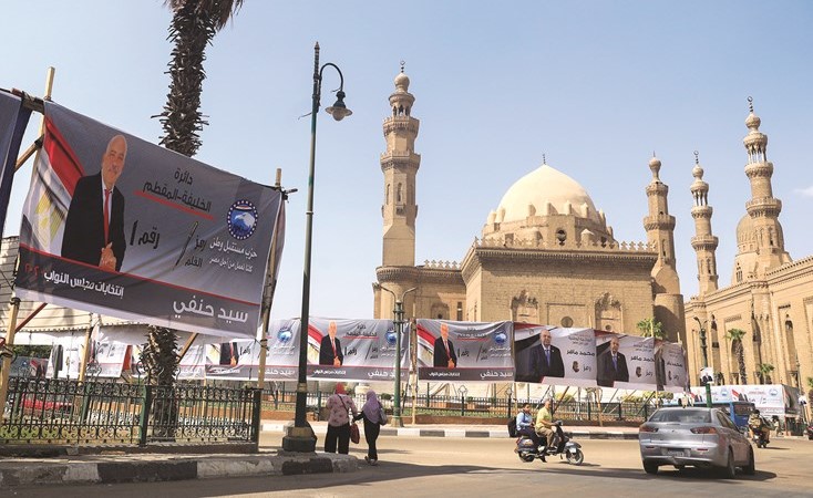 مصريون يمرون بالقرب من لافتات انتخابية أمام مسجد السلطان حسن بالقاهرة(رويترز)