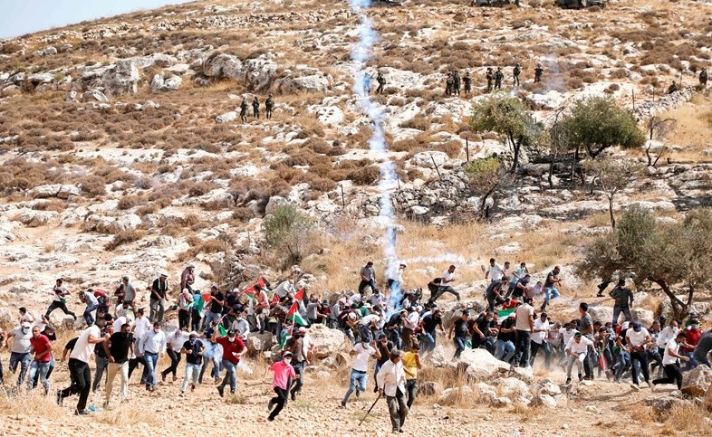 فلسطينيون يحتمون من قنبلة مسيلة للدموع ألقاها جنود الاحتلال عليهم خلال احتجاج على الاستيطان بالضفة امس(أ.ف.پ)