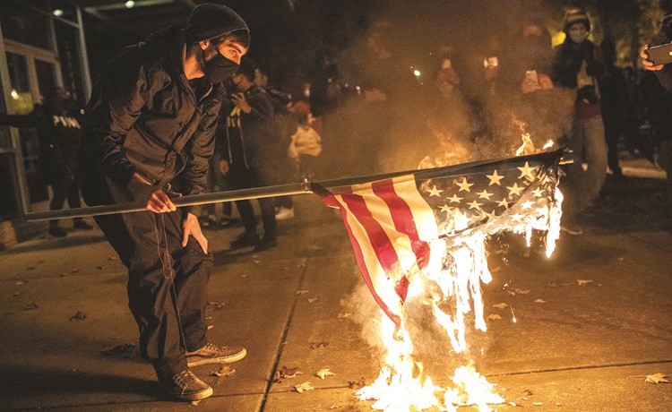 متظاهر يحرق العلم الاميركي في ڤانكوڤر احتجاجا على قتل الأميركي من أصول أفريقية كيفين بيترسون	(أ.ف.پ)