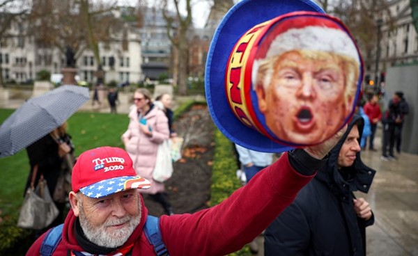 متظاهر بريطاني معارض للقاحات كورونا يحمل قبعة عليها صورة ترامب (رويترز)