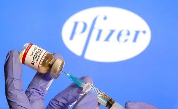 زجاجة صغيرة عليها ملصق "لقاح فيروس كورونا أمام شعار شركة فايزر (رويترز)