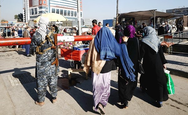 أفغانيات يسرن بجوار أحد عناصر طالبان الذي يتولى حراسة أحد أسواق العاصمة كابول أمس(رويترز)