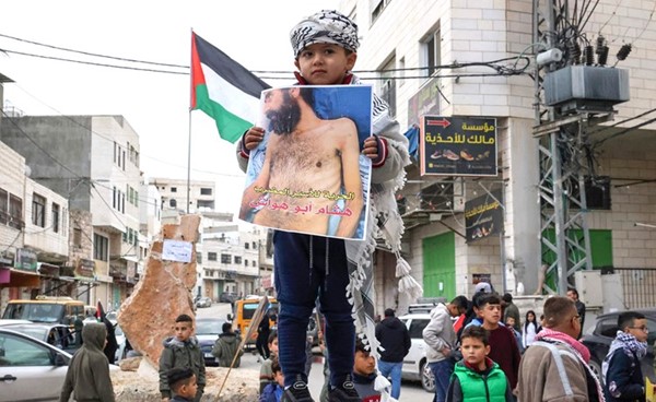 طفل فلسطيني يحمل صورة الأسير المضرب عن الطعام هشام أبو هواش في مسيرة في بلدته الدورا بالخليل (أ.ف.پ)