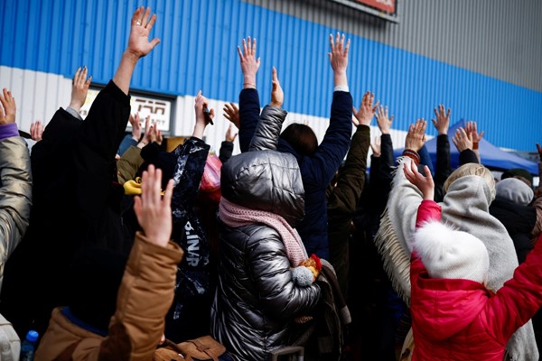  نازحون من أوكرانيا يلوحون بأيديهم قبل الصعود إلى حافلات لنقلهم إلى احد مراكز الإيواء في بولندا (رويترز) 