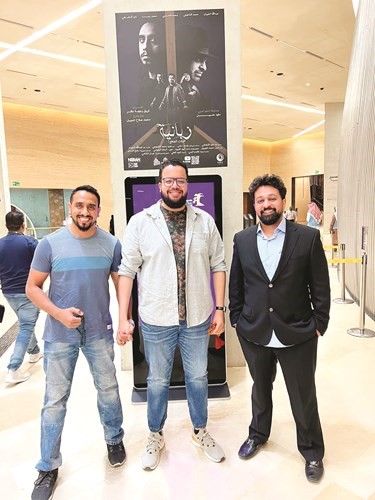 المخرج صلاح المجيبل والفنانان عبدالله الجيران ومحمد الشايجي أمام بوستر فيلمهم زبانية في سينما مركز إثراء
