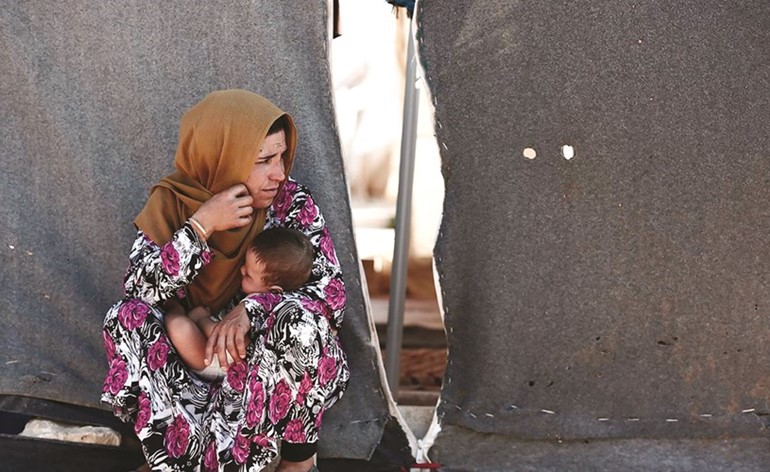 امرأة تحمل طفلها وتجلس قرب خيمتها في أحد مخيمات إدلب	(انترنت)