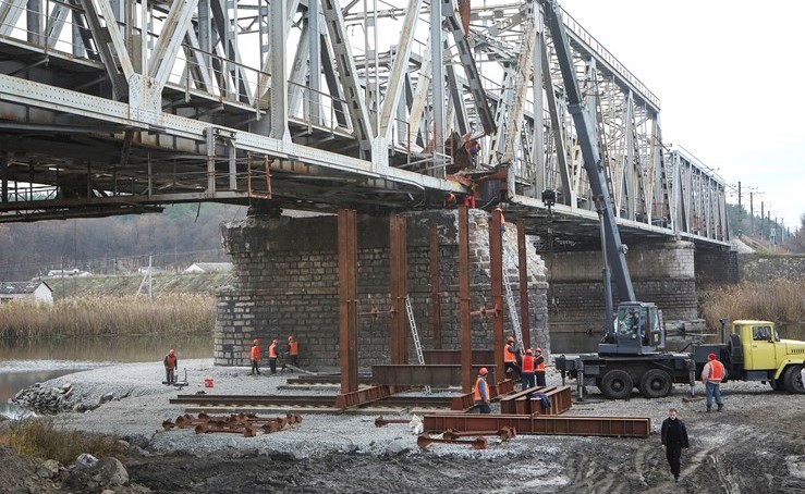 عمال يصلحون جسر السكك الحديدية المتضرر من الهجوم الروسي على أوكرانيا 	(رويترز)