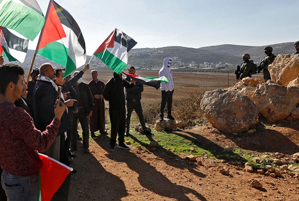 فلسطينيون يلوحون بعلم بلدهم خلال مواجهات مع قوات الاحتلال في نابلس بالضفة الغربية (ا.ف.ب)