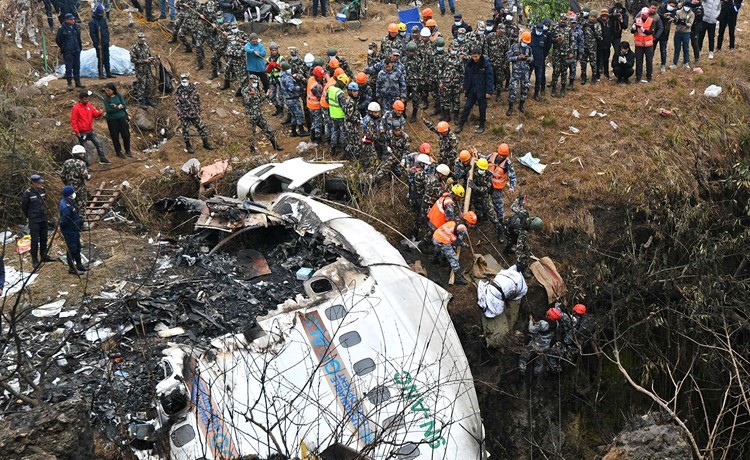 مسعفون يحملون جثمان احد ضحايا الطائرة النيبالية المنكوبة ويبدو جزء من حطامها (أ.ف.پ)