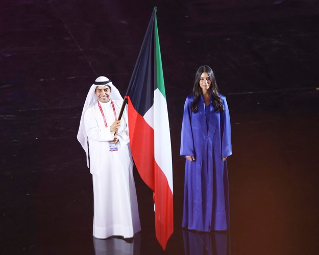 لاعب منتخبنا الوطني للرماية خالد المضف حاملا علم الكويت في حفل الافتتاح وإلى جانبه الفارسة يارا الهنيدي