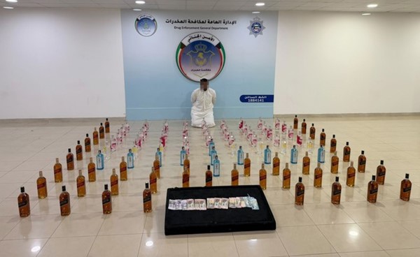 أحد المتهمين وأمامه 97 زجاجة من المشروبات الكحولية المستوردة و٥٢٠ دينار حصيلة بيع